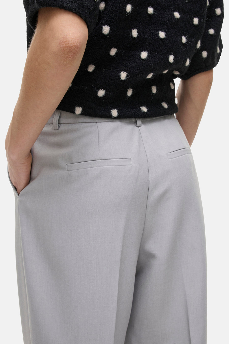 Grijze, wijde pantalon met achterzakken, gedragen met een zwarte trui met witte stippen.