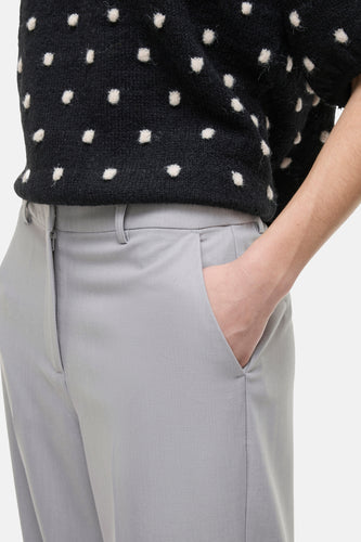 Grijze pantalon met hand in zak, zwart-witte trui.