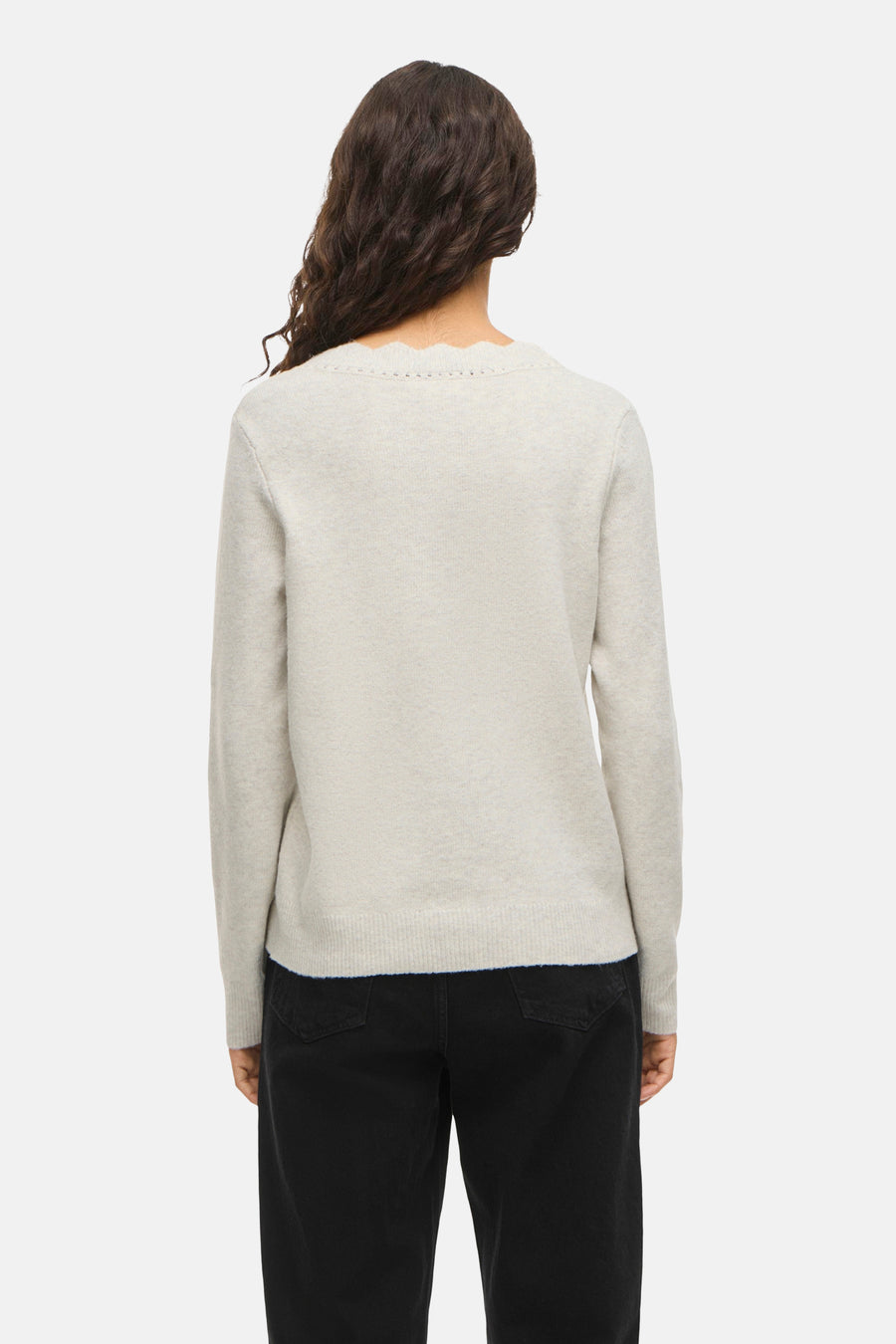 Achterkant van een vrouw in een grijze trui met zwarte jeans.