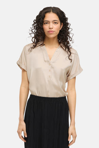 Blouse beige à manches courtes de VILA®, avec des boutons, associée à une jupe noire plissée.