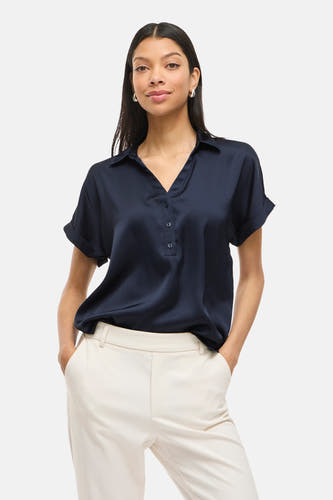 Blouse bleue à manches courtes de VILA®, avec fermeture à boutons et portée avec un pantalon crème.