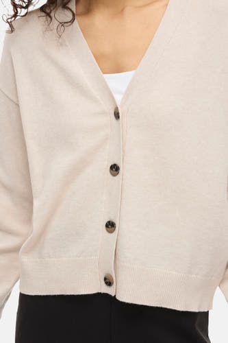 Cardigan écru de VILA® avec fermeture à boutons, porté sur un haut blanc et un pantalon noir.