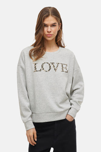 Pull-over gris de VILA, avec imprimé "LOVE" en motif de léopard, associé à des pantalons foncés et des chaussures en cuir.
