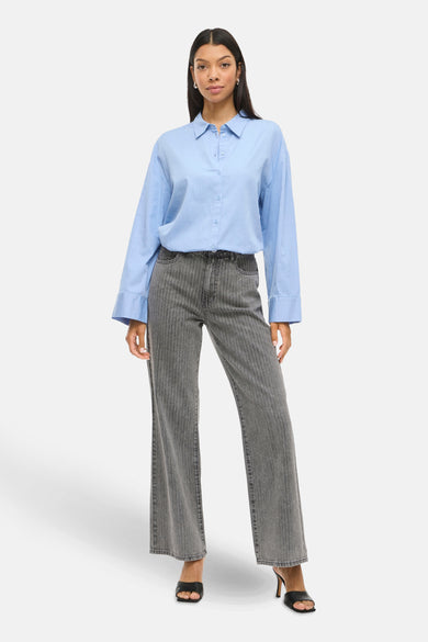 Jean wide bleu foncé de VILA, avec des rayures verticales et associé à une chemise bleue claire.