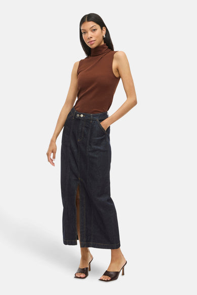 Jupe longue en denim bleu marine de VILA, avec une fente à l'avant, associée à une chemise brune et des bottes.