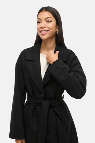 Manteau noir de VILA®, avec une ceinture et une fermeture à bouton unique, porté sur un chemisier blanc.