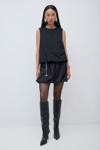 Jupe courte noire de VILA, portée avec une ceinture, un string et des bottes jusqu'aux genoux.