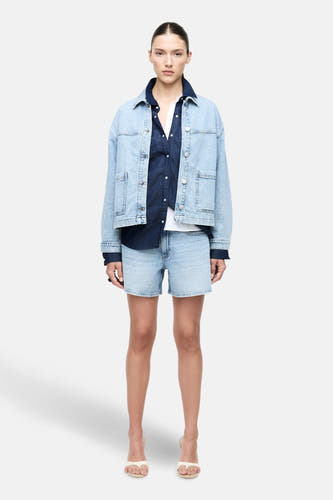 Veste en denim bleu clair de VILA®, associée à un chemisier bleu foncé et des shorts en denim.