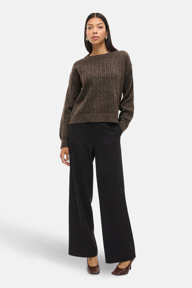 Bruine trui met ronde hals van VILA, met een grof gebreide textuur, gecombineerd met een zwarte, wijde pantalon en bruine pumps.
