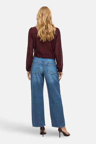 Jean bleu large de VILA, avec des poches arrière visibles et porté avec une blouse bordeaux.