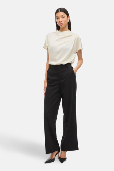 Blouse écru à manches courtes de VILA®, associée à des pantalons noirs larges et des escarpins.