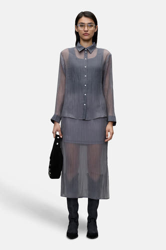 Chemise grise de VILA®, associée à une jupe grise et des bottes noires, avec un sac à main noir dans la main.
