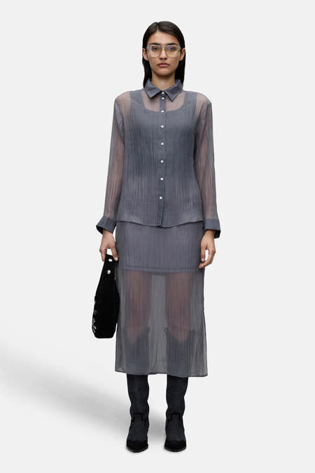 Chemise grise de VILA®, associée à une jupe grise et des bottes noires, avec un sac à main noir dans la main.