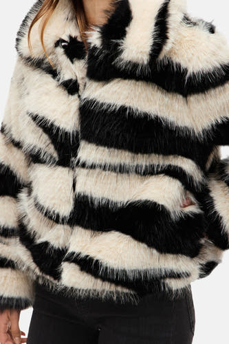 Manteau court en fourrure de VILA® avec motif zèbre, associé à des jeans skinny noirs et des bottes en cuir à talon.