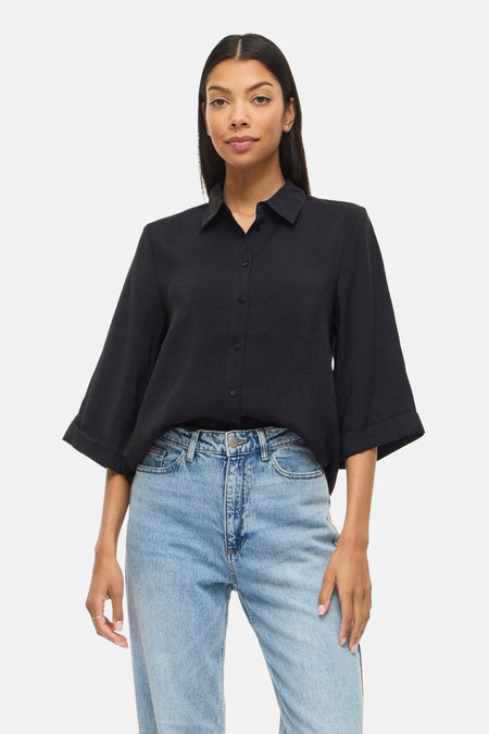 Chemise noire à manches courtes de VILA®, avec les bras croisés et un jean clair.