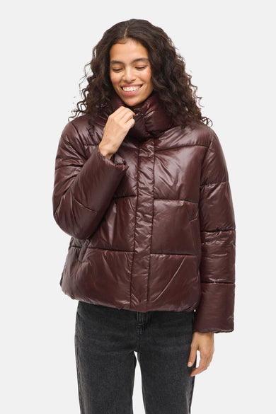 Bordeaux manteau court de Vila, avec une finition brillante et porté avec un jean noir.