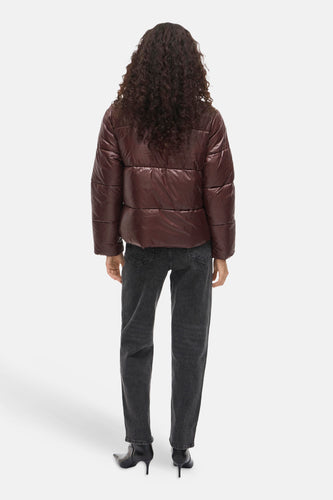 Achterkant van een vrouw in een bordeauxrode pufferjack, donkere jeans en zwarte laarzen.
