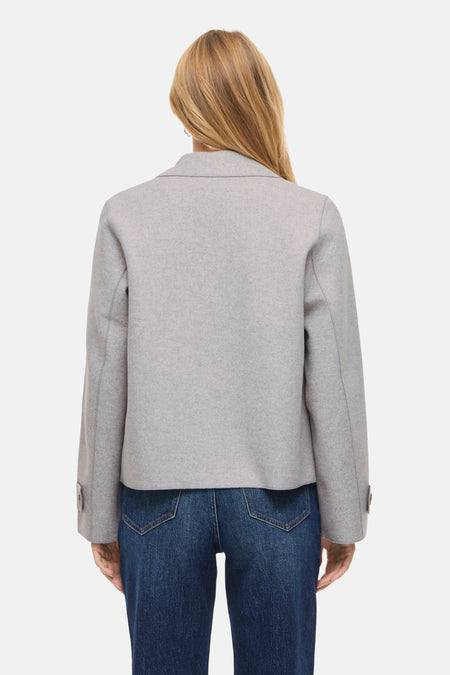 Grijs jasje met blauwe jeans, achteraanzicht.