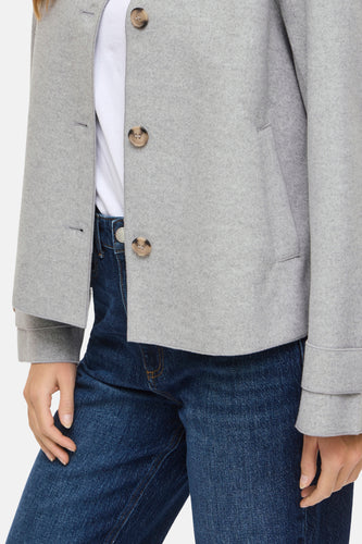 Grijze jas met knopen en blauwe jeans.
