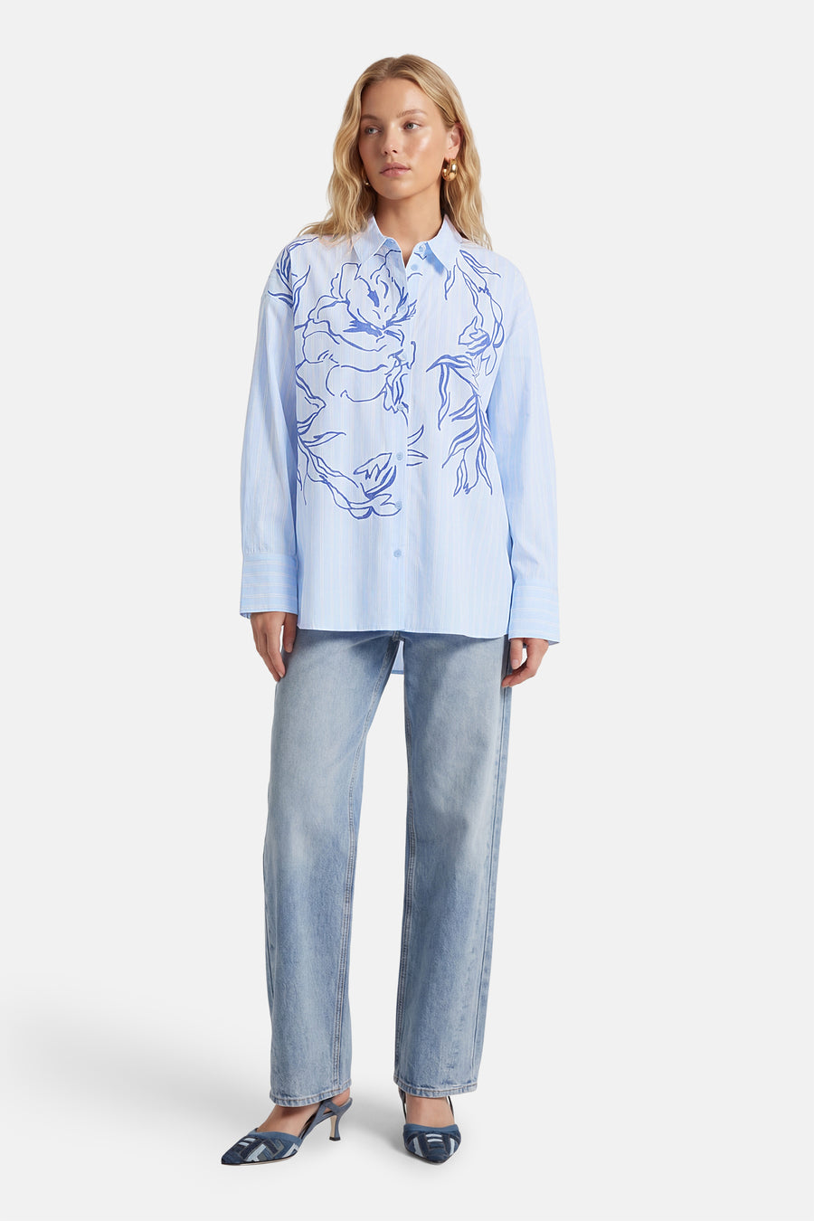 Blauw gestreept hemd met lange mouwen van Vila®, versierd met een blauwe bloemenprint, gedragen met jeans en hakken.
