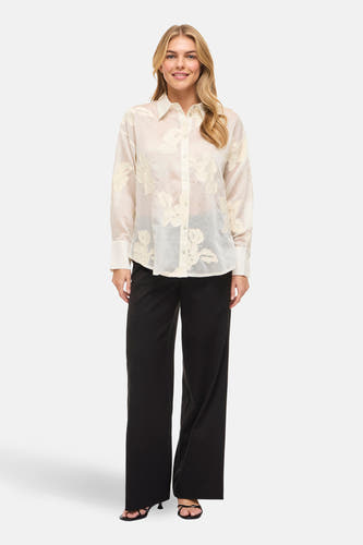 Chemise beige (manches longues) de Vila, avec détails floraux et associée à un pantalon noir et des talons.