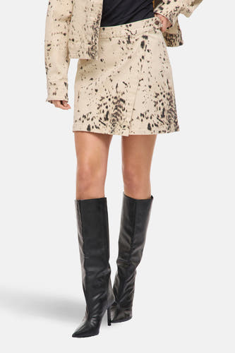 Jupe courte beige de VILA, avec un motif à pois marron foncé et une coupe asymétrique, portée avec des bottes noires.