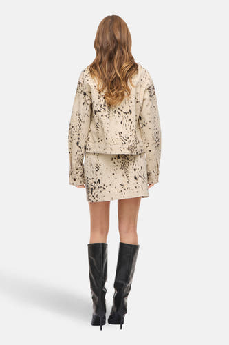 Jupe courte beige de VILA, avec un motif à pois noirs abstraits, combinée avec des bottes noires montantes jusqu'au genou.