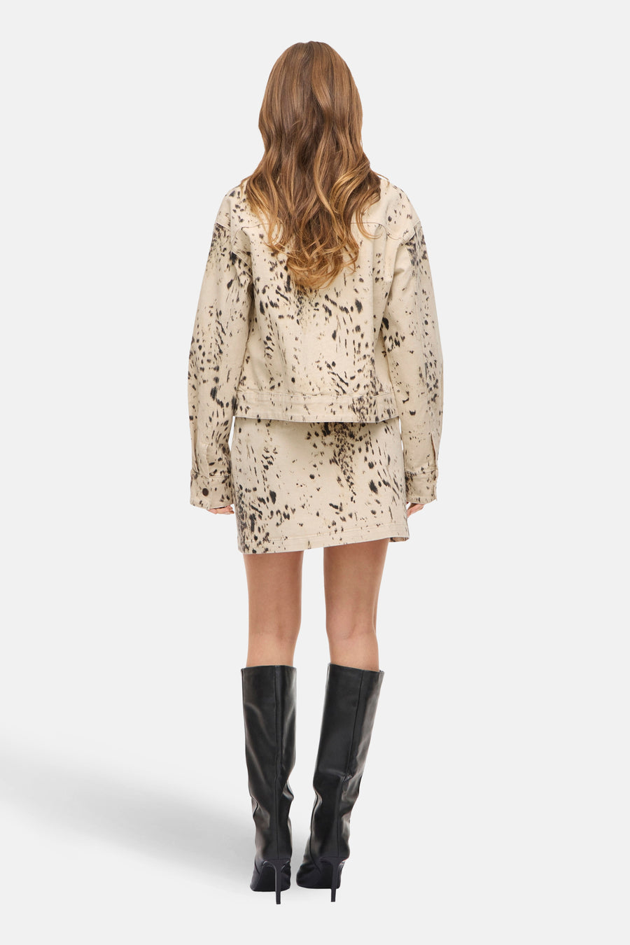 Jupe courte beige de VILA, avec un motif à pois noirs abstraits, combinée avec des bottes noires montantes jusqu'au genou.