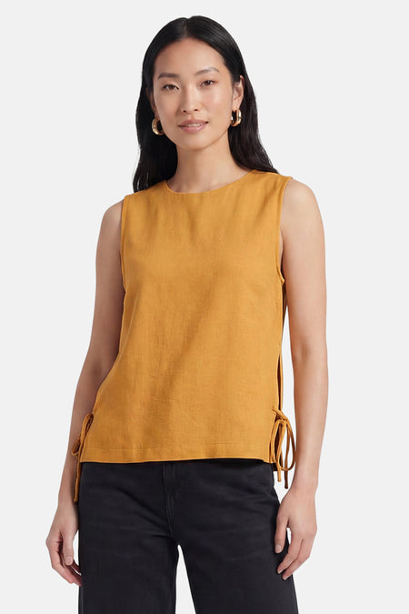 Chemisier sans manches jaune de VILA® avec détails de nœud sur le côté, porté avec un pantalon noir et des boucles d'oreilles dorées.