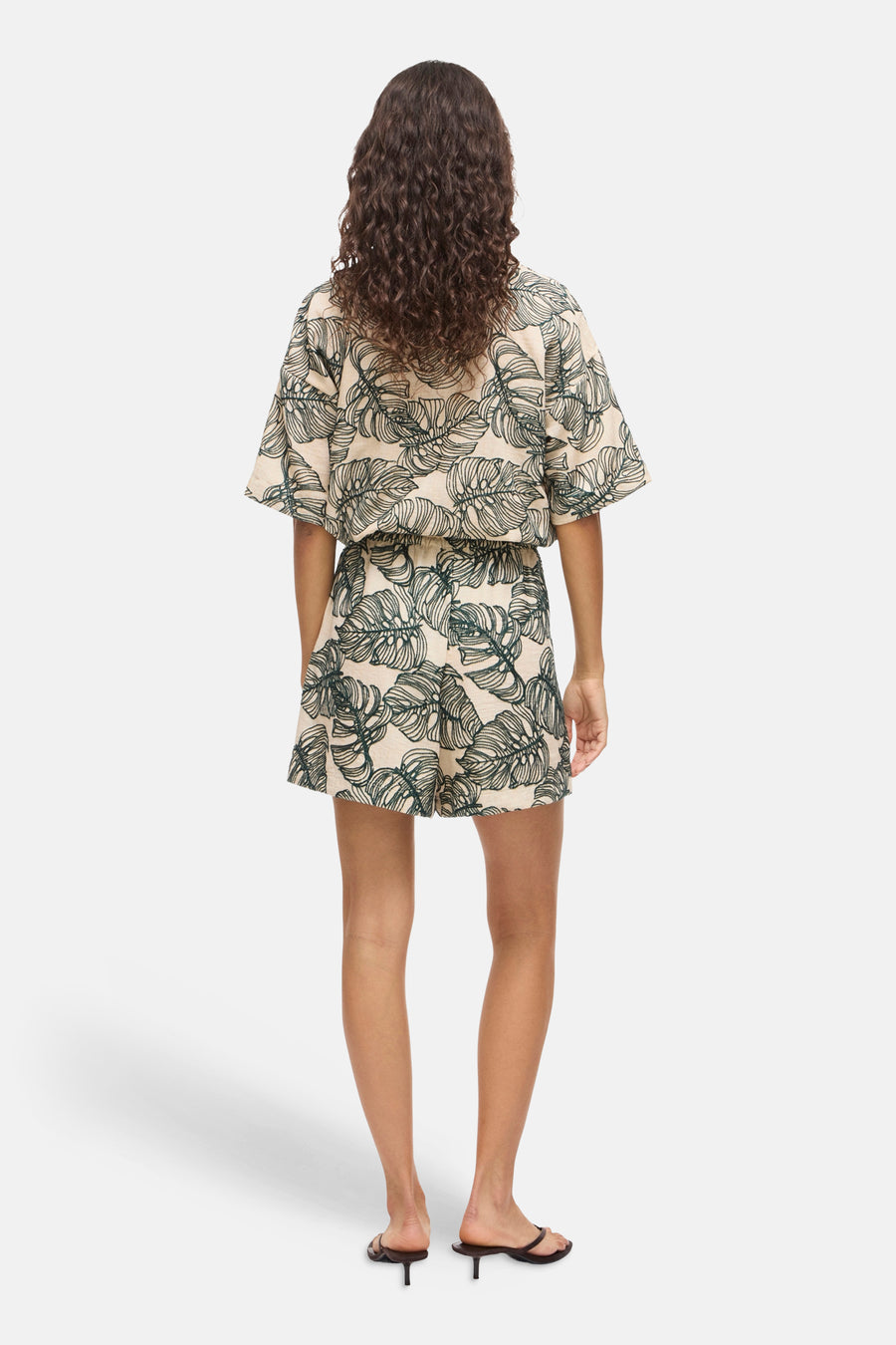 Short beige à motif de feuilles vertes de VILA, vu de dos avec un haut assorti et des sandales.