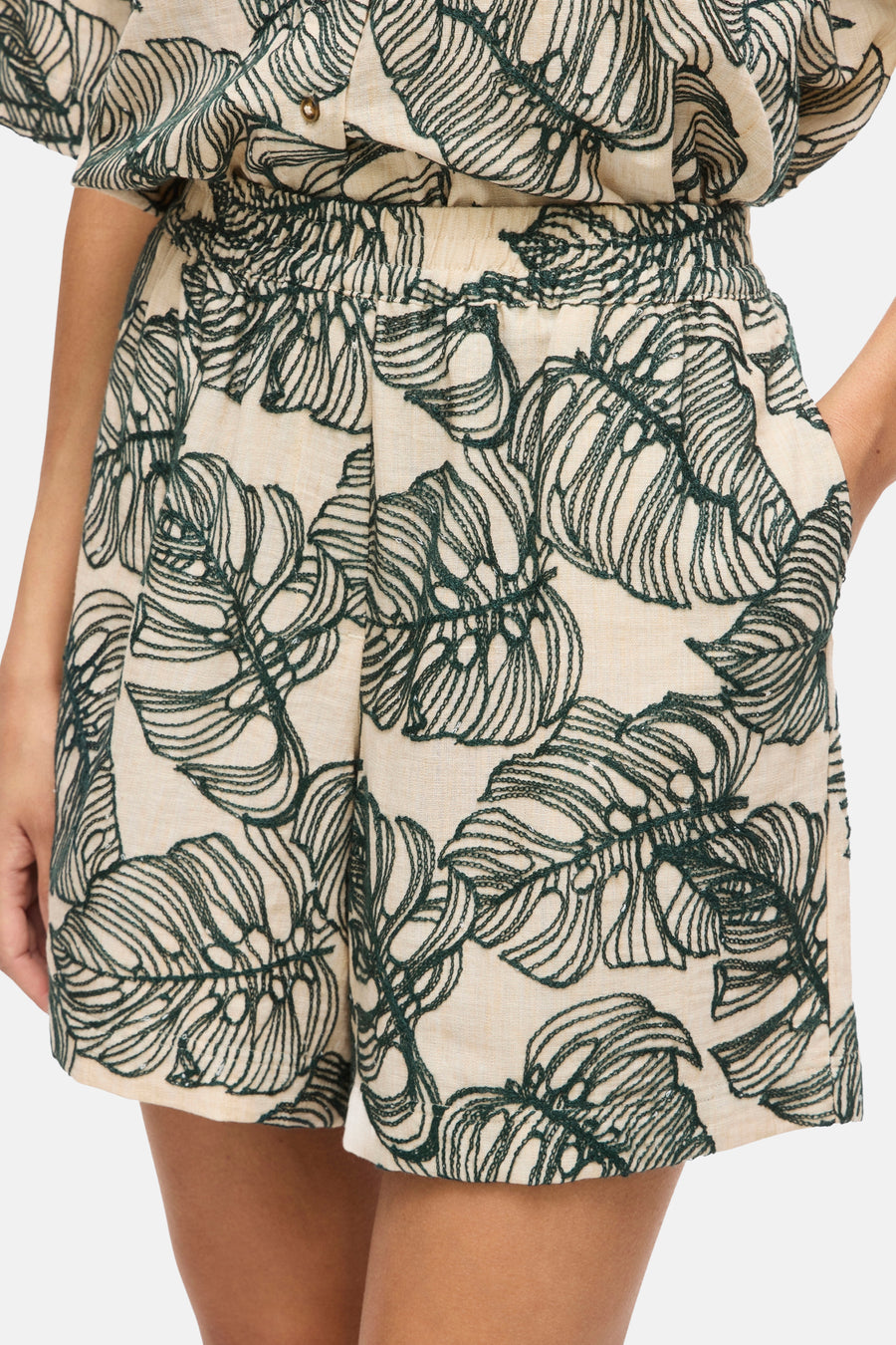 Short beige clair avec motif de feuilles brodé vert de VILA®, avec taille élastique et poches latérales, porté par un mannequin.