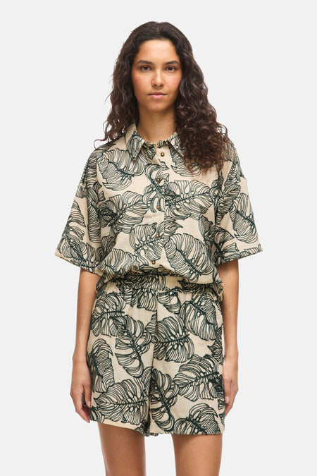 Chemise beige à manches courtes avec motif de feuilles vertes de VILA, combinée avec un short assorti et des sandales noires.