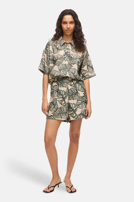 Beige hemd met korte mouwen en groen bladmotief van VILA, gecombineerd met bijpassende shorts en zwarte sandalen.