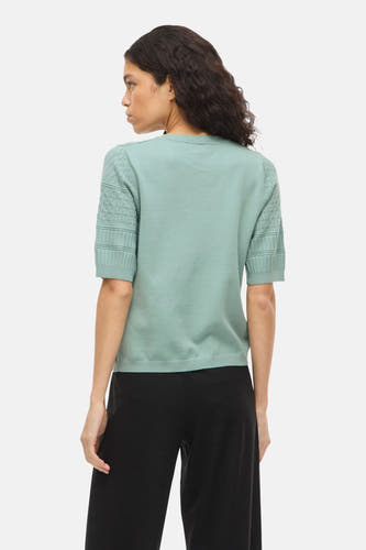 Pull vert avec col rond de VILA, avec manches courtes à motif losange et un pantalon noir uni.