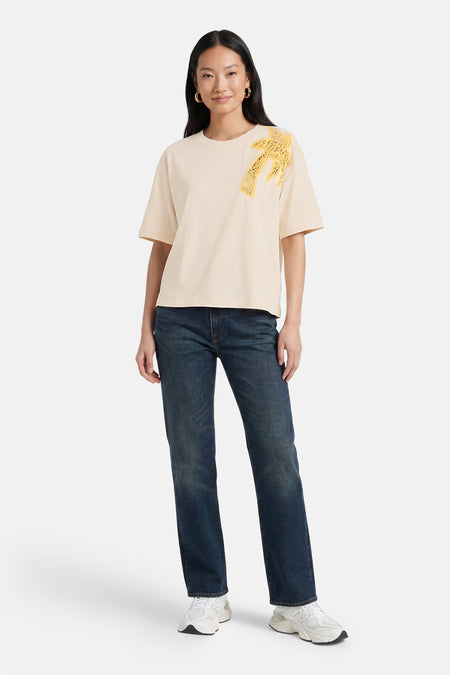 Beige korte mouwen T-shirt van VILA® met gele kant palmboom applicatie, casual fit, model draagt donkerblauwe jeans en witte sneakers