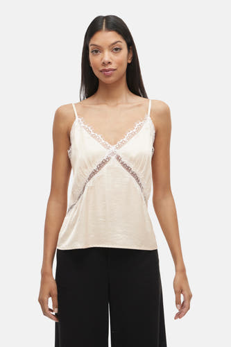 Blouse écru sans manches de VILA, avec des détails sur les bords, associée à une jupe noire large et à des sandales à talon.