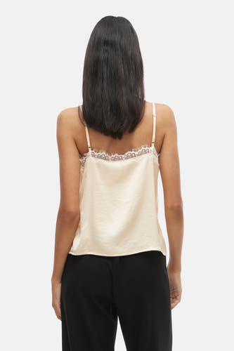 Blouse écru sans manches de VILA, avec des détails sur les bords, associée à une jupe noire.