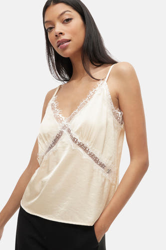 Blouse à manches courtes écru de VILA, avec des détails sur les bords le la ligne du cou et des côtés, associée à une jupe noire.