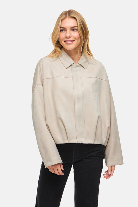 Beige korte jas van VILA, gedragen over een zwarte broek tegen een witte achtergrond.
