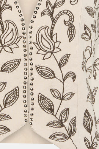 Gilet de couleur crème de VILA avec des clous argentés et une broderie florale marron foncé.