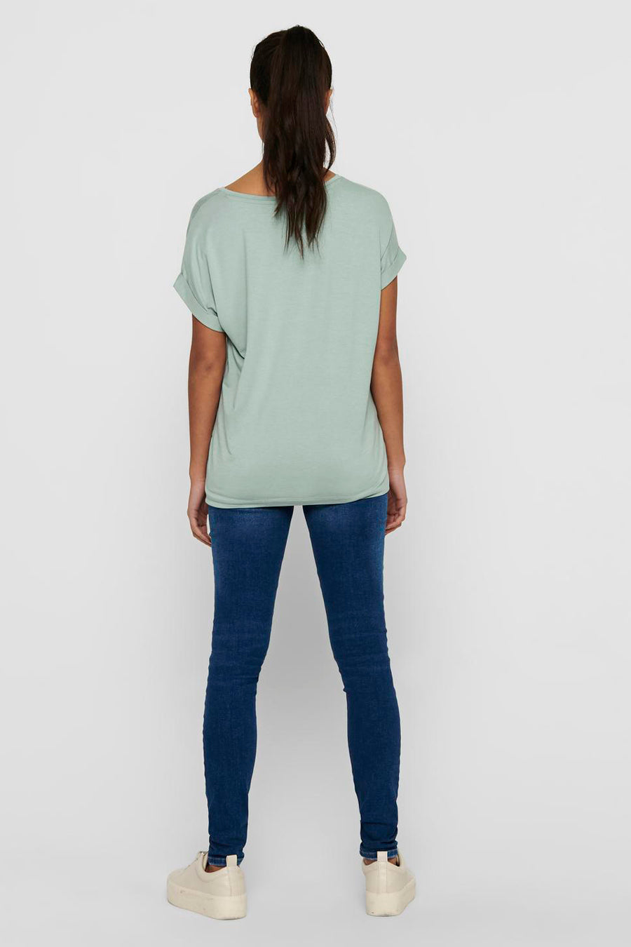 Dos d'une femme en un t-shirt vert clair, des jeans bleus et des chaussures beige.