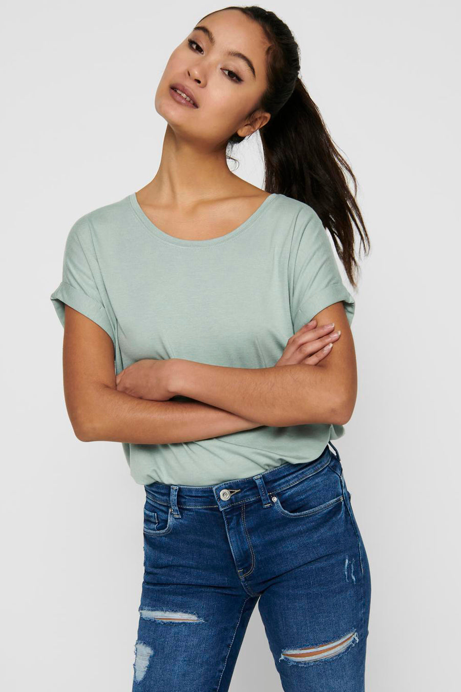Femme avec les bras croisés dans un t-shirt vert et des pantalons de travail bleus.