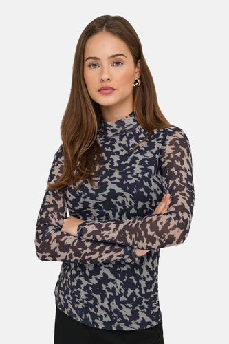 Vrouw met gekruiste armen, blouse met luipaardprint, gouden oorbellen.
