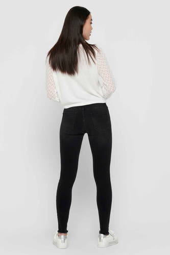 Zwarte skinny jeans van ONLY, met een gerafelde zoom, gecombineerd met een witte top met patroon.
