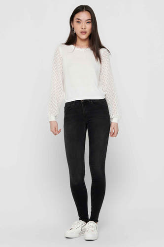 Jean skinny noir ONLY, avec des longues pattes et porté avec un haut blanc et des baskets.