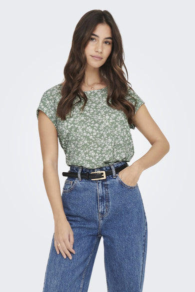 Blouse verte à manches courtes d'ONLY, avec un imprimé de fleurs blanches, combinée avec une ceinture noire et un jean.