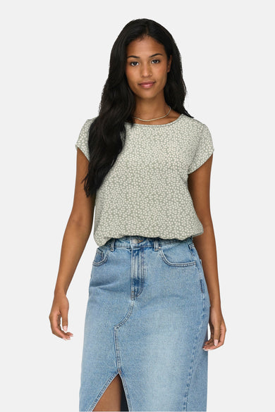Blouse verte avec des manches courtes de ONLY, avec un motif de feuille blanche, portée avec un pantalon crème et des chaussures noires.