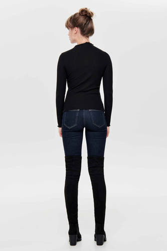 Pull noir ONLY, avec des manches longues, associé à un jeans foncé et des bottes noires hautes.