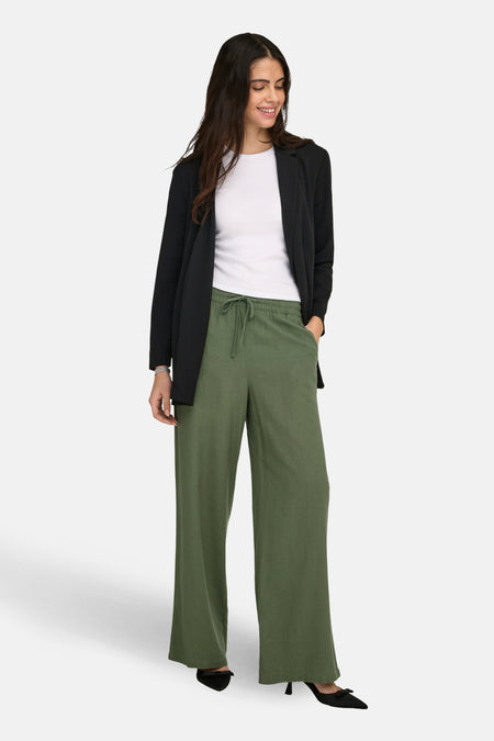 Femme avec un blazer noir, une chemise blanche, un pantalon vert et des chaussures noires.