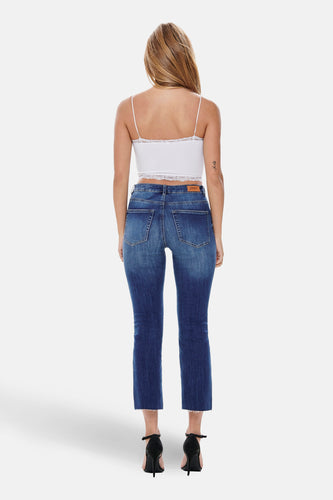 Achterkant van een vrouw met een witte top en blauwe jeans, staand op zwarte hakken tegen een witte achtergrond.